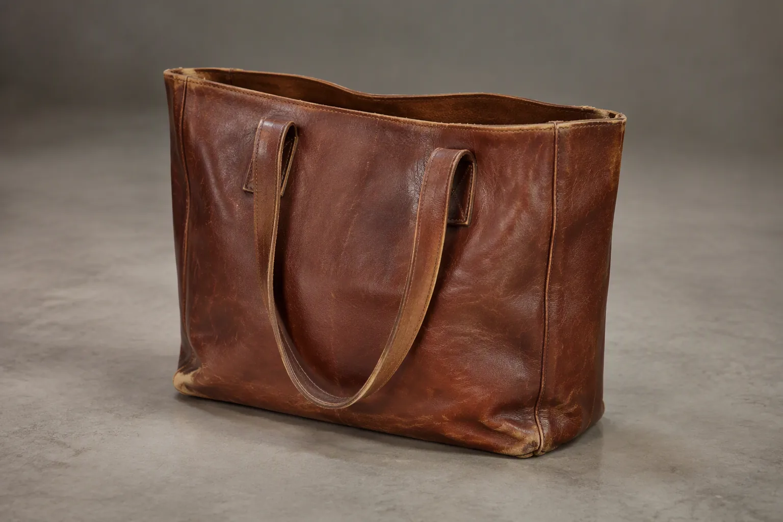 A well-used leather tote photographed for inspection, with wear at the top edge, handle roots and base corners