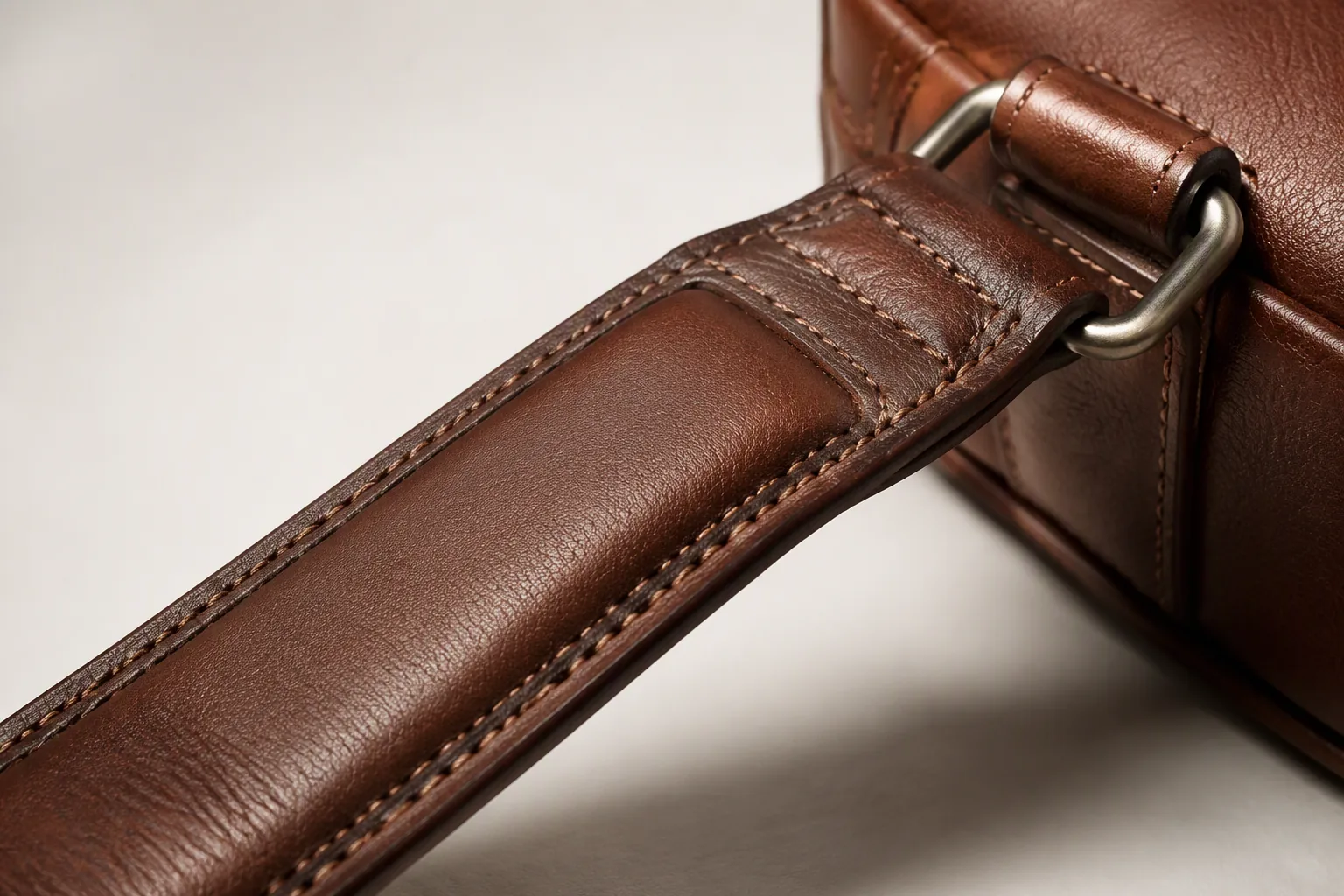 A padded leather shoulder strap with stitching and a reinforced anchor